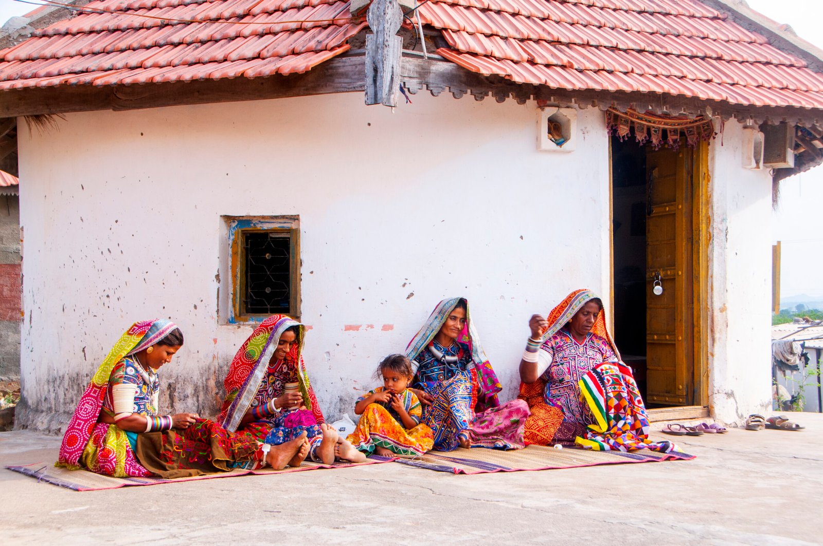 Tribal women sewing ethnic and traditional hand embroidered dresses in front of their hut, Gujarat, India.